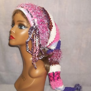 May include: A handmade, colorful crochet hat with a long, pointed tail and dangling tassels. The hat features a mix of pink, purple, white, and other vibrant colors. The hat has a pom-pom at the end of the tail.