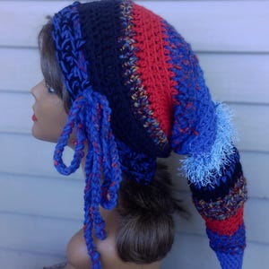 May include: A handmade, colorful crochet hat with a long, pointed tail. The hat features sections of red, navy blue, and lighter blue yarn, with decorative tassels and fringe. The hat is designed to be worn on the head.