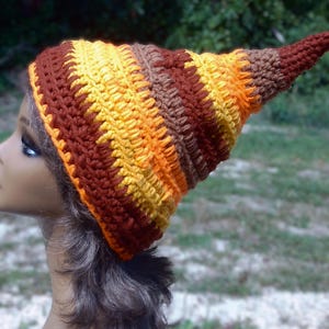 May include: A handmade crochet hat with a pointed top. The hat features horizontal stripes of brown, yellow, and orange. The hat is displayed on a mannequin head.