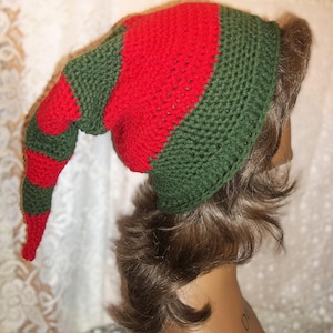 May include: A red and green striped elf hat with a long pointed tip. The hat is crocheted and has a green base with red stripes.