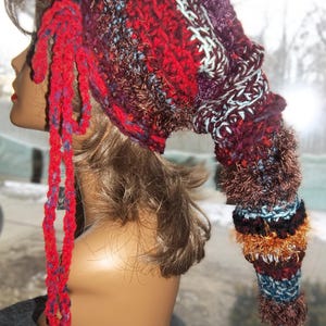 May include: A red, brown, purple, and white crocheted hat with a long, colorful tail. The hat has a long, red crocheted tie.