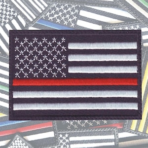 May include: A black and white American flag patch with a red stripe across the middle. The flag is embroidered with white stars and stripes on a dark blue background.