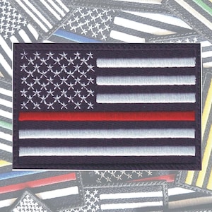 May include: Embroidered patch featuring an American flag design with a red stripe, white stars, and white stripes on a black background. The image shows several similar patches with different colored stripes.