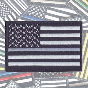 May include: A black and white American flag patch with a thin blue line across the middle. The patch is embroidered with white thread on a black background.