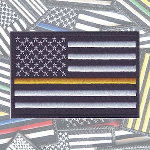 May include: A black and white American flag patch with a thin gold stripe across the middle. The patch is embroidered and has a black border.