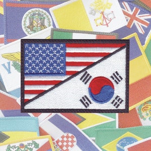 May include: A patch with the American flag on the left and the South Korean flag on the right, both flags are sewn together diagonally. The patch is surrounded by a black border and is on a background of many different country flags.