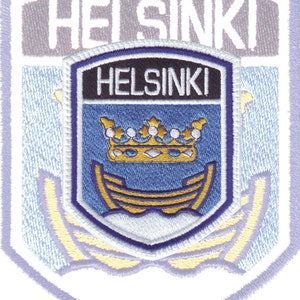 May include: A blue and white embroidered patch with the word "HELSINKI" in white lettering. The patch features a blue shield with a gold crown and a gold ship.