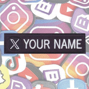May include: A black and white embroidered patch with a white "X" and the text "YOUR NAME" in white on a black background.