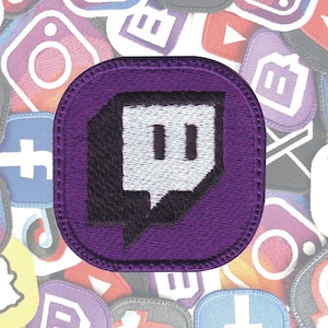 Peut inclure: Un écusson brodé violet avec le logo Twitch, une bulle de dialogue blanche avec deux rectangles verticaux. L'écusson est entouré d'autres écussons de logos de médias sociaux, dont Instagram, Facebook et YouTube. Les écussons sont probablement pour les vêtements ou les accessoires.