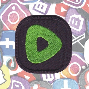 May include: A dark purple embroidered patch with a green play button icon. The patch is surrounded by other colorful patches, including social media logos.