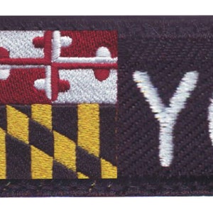 May include: A black embroidered patch with the Maryland state flag and the text "YOUR NAME" in white.