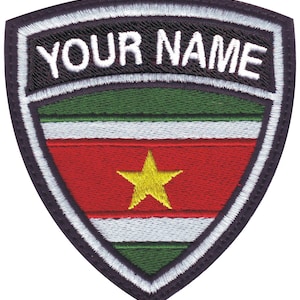 May include: A black and white embroidered patch with a shield shape. The shield has a green, white, red, and green striped design with a yellow star in the center. The text "YOUR NAME" is embroidered in white on a black background at the top of the shield.