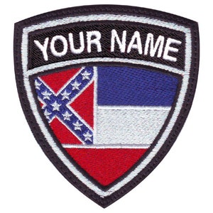 May include: A black and white embroidered patch in the shape of a shield. The shield features the Confederate flag and the text "YOUR NAME".