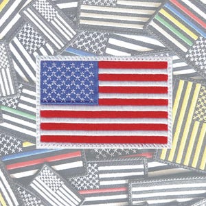 May include: Embroidered patch featuring the American flag with red and white stripes and a blue field of white stars. The patch is rectangular with a white border. Other flag patches are in the background.