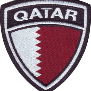 May include: A white and maroon embroidered patch with the word "QATAR" in white lettering on a black background.