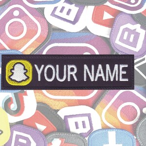 May include: A purple and white embroidered patch with a white ghost icon inside a yellow circle and the text "YOUR NAME" in white.