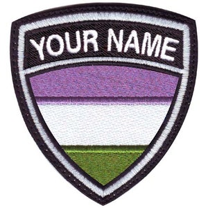 May include: A black and white embroidered patch in the shape of a shield with a purple, white, and green striped flag inside. The text "YOUR NAME" is embroidered in white on a black background at the top of the patch.