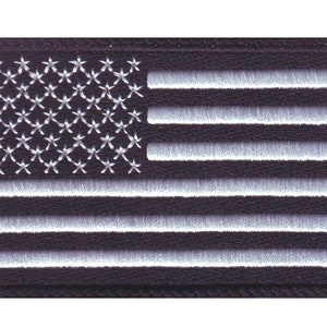 May include: A black embroidered patch with a white American flag design. The flag has 13 horizontal stripes and 50 white stars in a blue field.