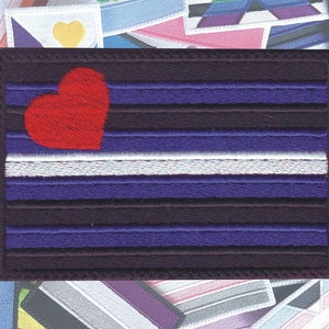May include: A dark purple and white embroidered patch with a red heart in the top left corner. The patch has five horizontal stripes, with the top stripe being the largest and the bottom stripe being the smallest. The patch is surrounded by a black border.