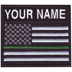 May include: Black and green embroidered patch with a white American flag and the text "YOUR NAME" above the flag.