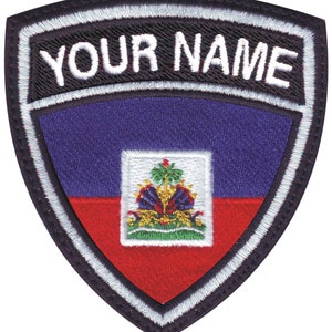 May include: A black and white embroidered patch with a shield shape. The shield features the flag of Haiti with the coat of arms in the center. The text "YOUR NAME" is embroidered in white on a black background above the shield.