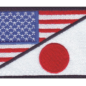 May include: A patch with the American flag and the Japanese flag, both sewn together in a diagonal pattern. The American flag is on the left side of the patch and the Japanese flag is on the right side. The flags are both embroidered in white, red, and blue thread.