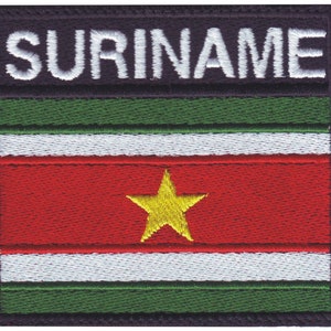 May include: Embroidered patch with the word "SURINAME" in white text on a black background. The patch features the flag of Suriname, with green, white, red, and yellow colors.