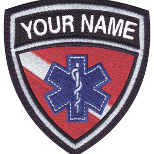 Peut inclure: Écusson brodé avec un fond rouge et blanc, une étoile de vie bleue avec un caducée blanc, et le texte "YOUR NAME" en lettres blanches sur fond noir.