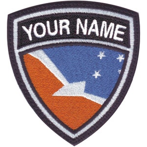May include: A black and white embroidered patch with a blue, white, and orange flag design. The text "YOUR NAME" is embroidered in white on a black background.