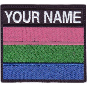 May include: A black and white embroidered patch with the text "YOUR NAME" in white lettering. The patch features three horizontal stripes in pink, green, and blue.