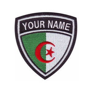 May include: A black and white embroidered patch with a green and white shield shape. The shield has the Algerian flag with a red crescent moon and star. The text "YOUR NAME" is above the shield.