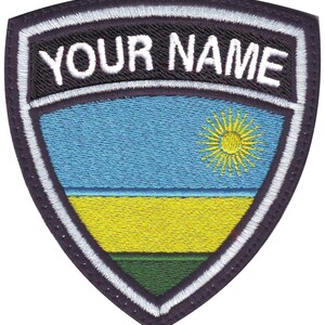 May include: An embroidered patch featuring the flag of Rwanda in a shield shape with a white border. The patch has a black background with white text that reads "YOUR NAME".