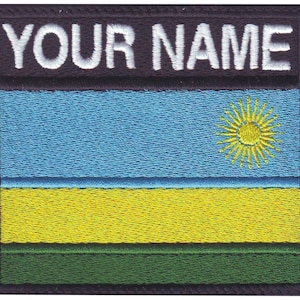 May include: Embroidered patch with the text "YOUR NAME" in white letters on a black background. The patch features the flag of Rwanda with a blue, yellow, and green horizontal stripe design. A yellow sun is in the upper right corner of the blue stripe.