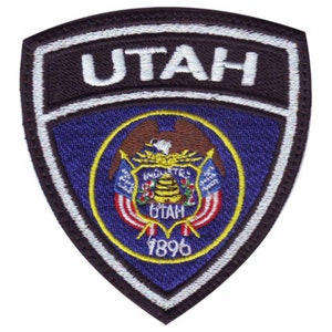May include: A black and white embroidered patch with the word "UTAH" in white lettering. The patch features the state seal of Utah, which includes a beehive, a bald eagle, and the words "Industry" and "State of Utah". The seal is surrounded by a blue circle with a yellow border and the year "1896" in yellow lettering.