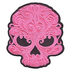 May include: Pink embroidered skull patch with intricate floral designs. The skull has black eyes and a black outline.