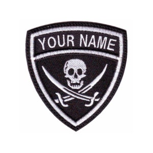 May include: Black and white embroidered patch with a skull and crossbones design. The patch has a white border and the text "YOUR NAME" in white lettering.