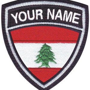 May include: A black and white embroidered patch with a red, white, and green Lebanese flag in the center. The text "YOUR NAME" is embroidered in white on a black background above the flag.