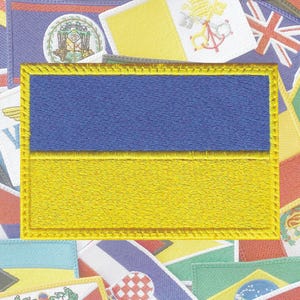 May include: A close-up of a yellow and blue embroidered patch depicting the flag of Ukraine. The patch is surrounded by other colorful patches, creating a vibrant background.