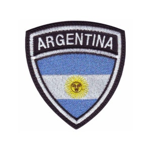 May include: An embroidered patch featuring the Argentinian flag in a shield shape with the word "ARGENTINA" above the flag. The flag is blue and white with a yellow sun in the center.