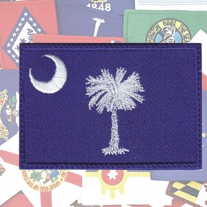 May include: A blue embroidered patch with the state flag of South Carolina. The flag features a white crescent moon and a palmetto tree on a blue background.