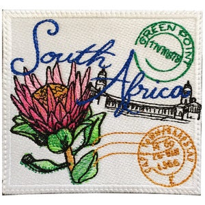 May include: Embroidered patch with a white background featuring a pink and green protea flower, a blue and white building, and the text "South Africa" in blue. The patch also has two green and gold stamps with the text "Green Point" and "Cape Town" respectively.