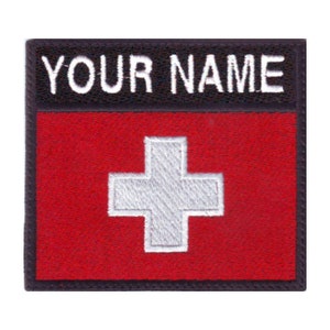 May include: A black and red embroidered patch with a white cross in the center. The text "YOUR NAME" is at the top of the patch.