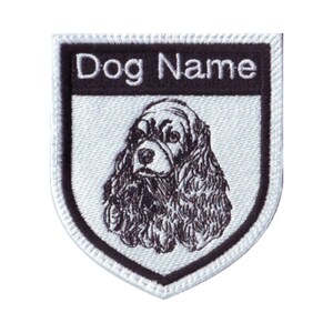 May include: White embroidered patch with a black border. The patch features a black and white illustration of a Cocker Spaniel dog's head. The text "Dog Name" is embroidered in white on a black background at the top of the patch.