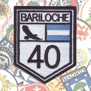 May include: A navy blue embroidered patch with a white background. The patch features the text "BARILOCHE" in white lettering, a black silhouette of a bird, a blue and white flag, and the number "40" in white.