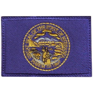 May include: A purple embroidered patch with the state seal of Nebraska. The seal features a gold outline and the words "Great Seal of the State of Nebraska" and "March 1st 1867".