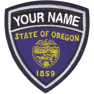 May include: A purple and black embroidered patch with the text "STATE OF OREGON" and "1859" in gold. The patch also features a gold seal with a sun and a mountain range. The text "YOUR NAME" is at the top of the patch.