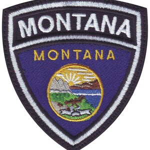 May include: A blue and white embroidered patch with the word "MONTANA" in white lettering and the state seal of Montana in the center. The seal features a mountain range, a sun, a river, and a grizzly bear.