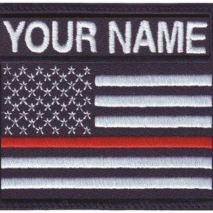 May include: Embroidered patch featuring a stylized American flag design with a red stripe. The top section displays the text "YOUR NAME" in white thread. The patch has a black background and a stitched border.