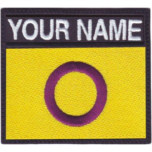 May include: A yellow embroidered patch with a purple circle in the center. The patch has a black border and the text "YOUR NAME" in white lettering at the top.