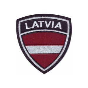 May include: Embroidered patch featuring the Latvian flag in red and white with a black outline. The word "LATVIA" is embroidered in white on a black background above the flag.
